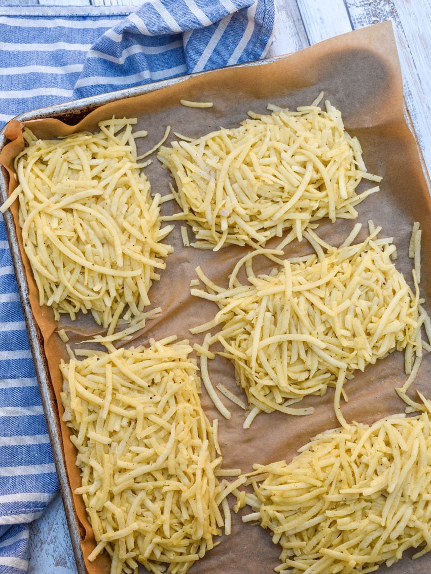 shredded seasoned potatoes shaped into hashbrown patties on a parchment paper lined baking sheet