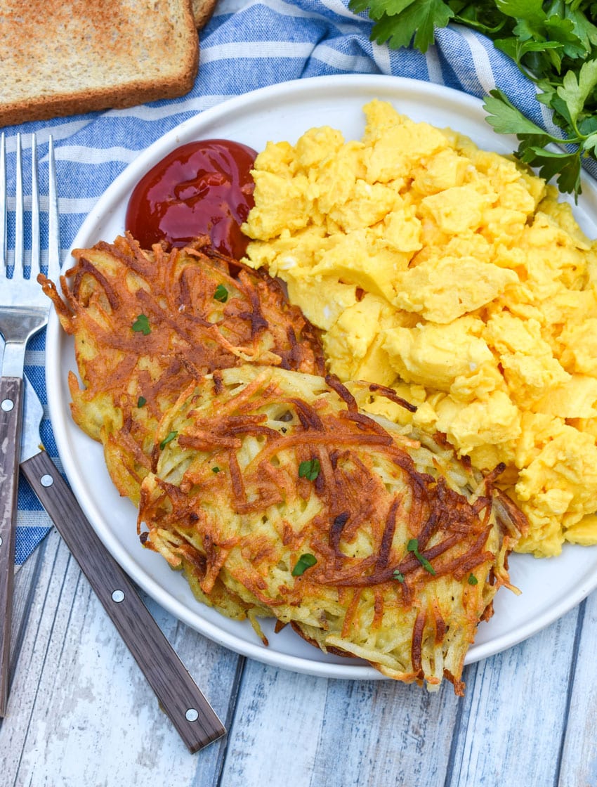 two homemade hash brown patties next to scrambled eggs on a white plate