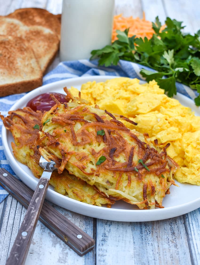 two homemade hash brown patties next to scrambled eggs on a white plate