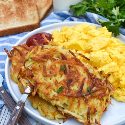 two homemade hash brown patties next to scrambled eggs on a white plate