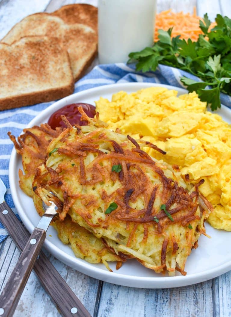 two homemade hash brown patties next to scrambled eggs on a white plate