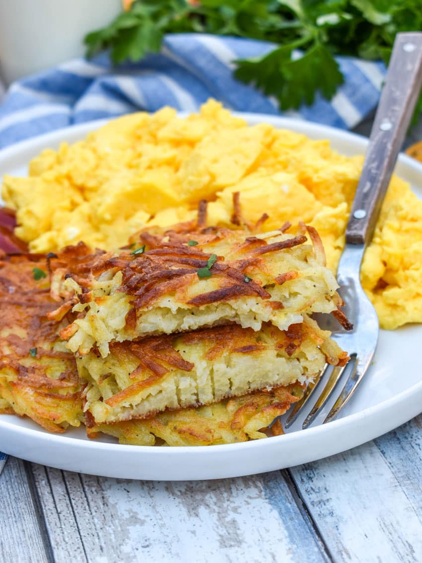 crispy homemade hash brown patties next to scrambled eggs on a white plate