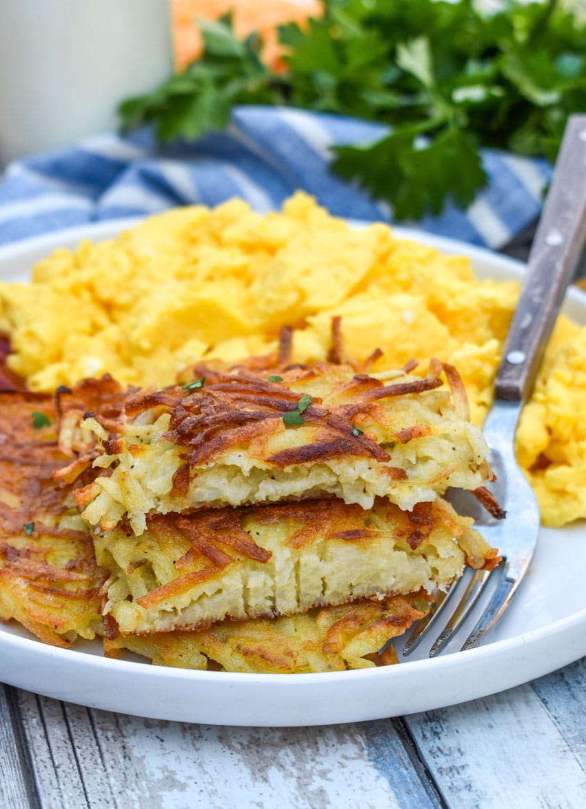 crispy homemade hash brown patties next to scrambled eggs on a white plate
