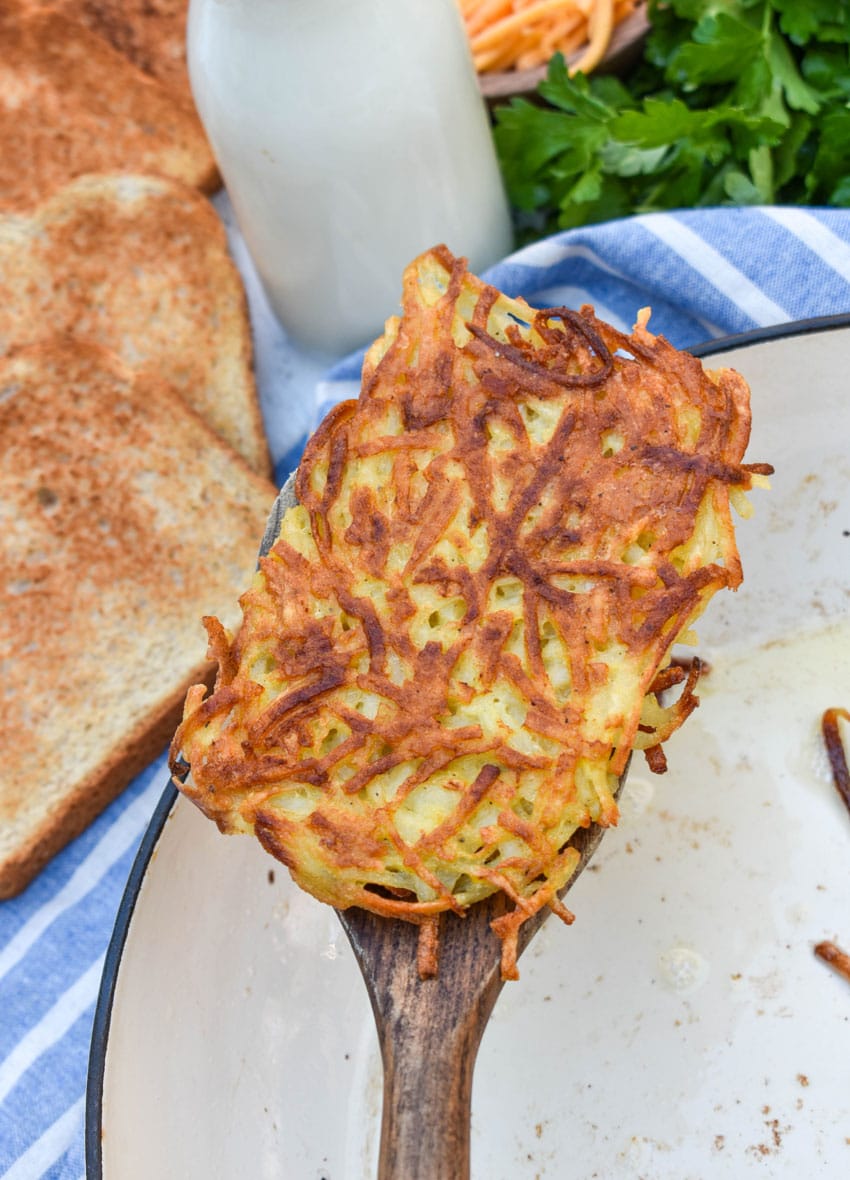 a wooden spatula holding up a crispy pan fried homemade hash brown patty