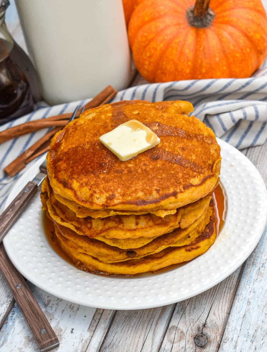 a stack of homemade pumpkin pancakes topped with syrup and a pat of butter on a small white plate