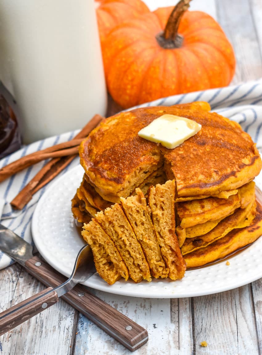a silver fork holding up a cut wedge of a stack of pumpkin pancakes