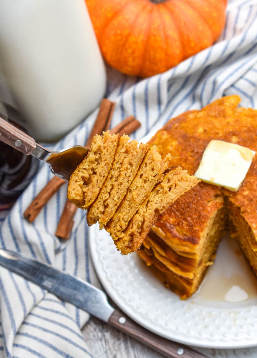 a fork holding up a cut wedge of a stack of pumpkin pancakes