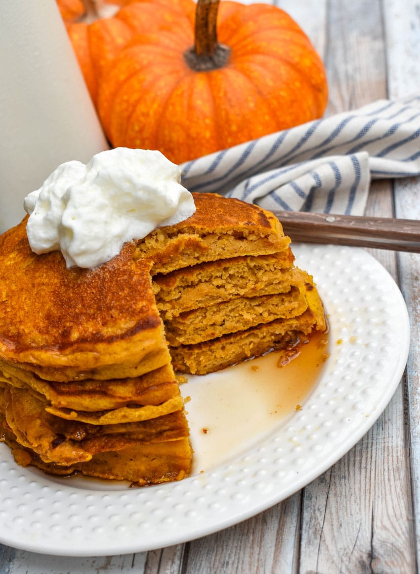 a stack of homemade pumpkin pancakes topped with syrup and a pat of butter on a small white plate