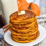a stack of homemade pumpkin pancakes topped with syrup and a pat of butter on a small white plate