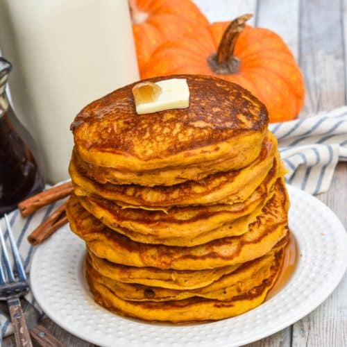 a stack of homemade pumpkin pancakes topped with syrup and a pat of butter on a small white plate