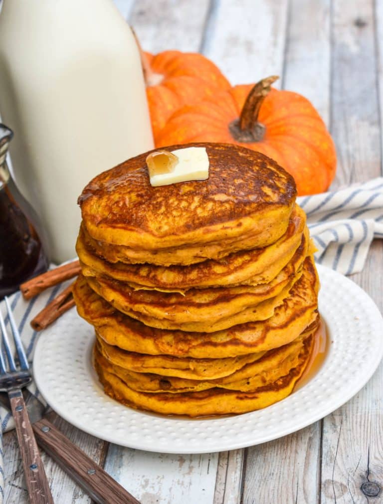 a stack of homemade pumpkin pancakes topped with syrup and a pat of butter on a small white plate