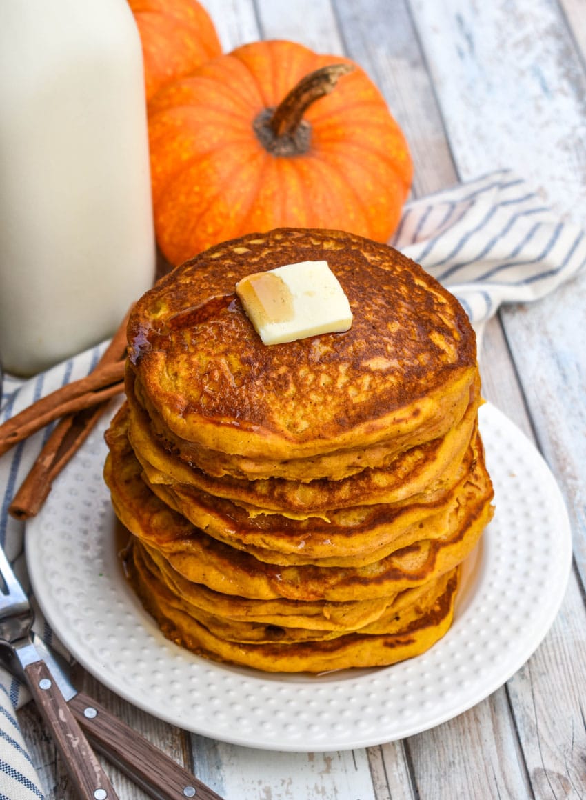 a stack of homemade pumpkin pancakes topped with syrup and a pat of butter on a small white plate