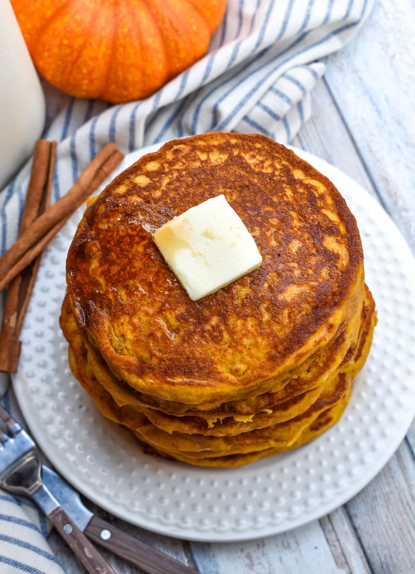 a stack of homemade pumpkin pancakes topped with syrup and a pat of butter on a small white plate