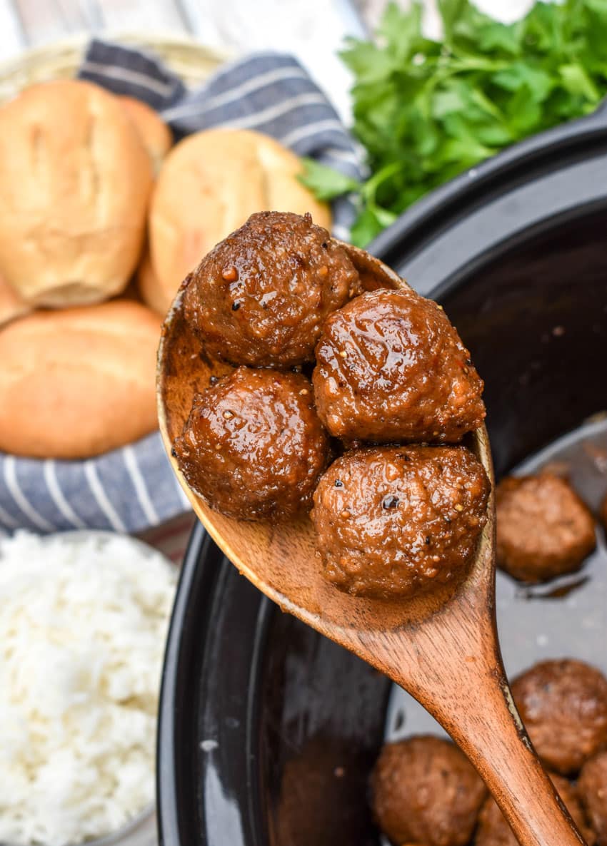 a wooden spoon holding up a scoop of slow cooked brown sugar meatballs