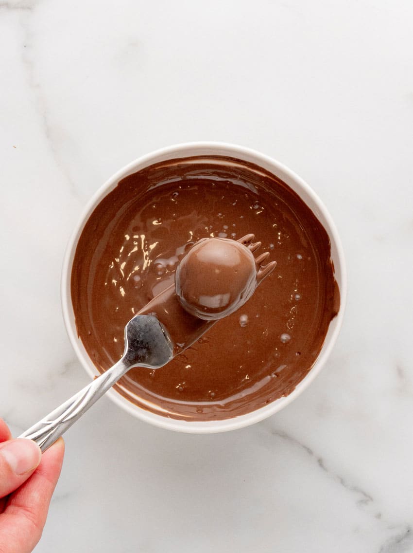 a silver fork lifting up a butterfinger truffle coated in melted chocolate