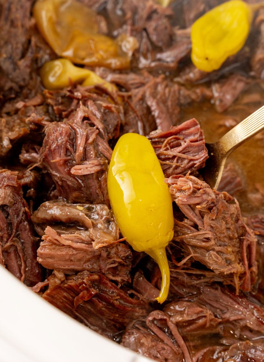 shredded mississippi pot roast and pepperoncini peppers in the bowl of a white slow cooker