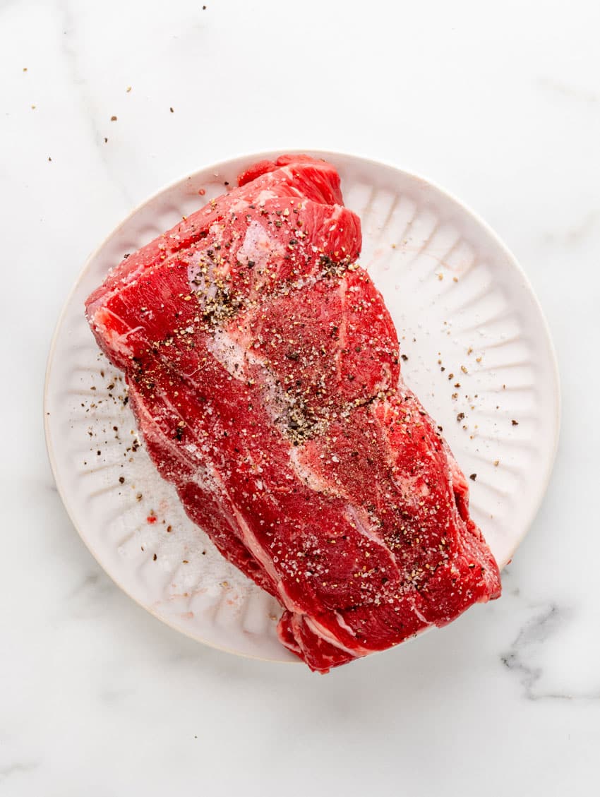 a seasoned uncooked chuck roast on a white plate
