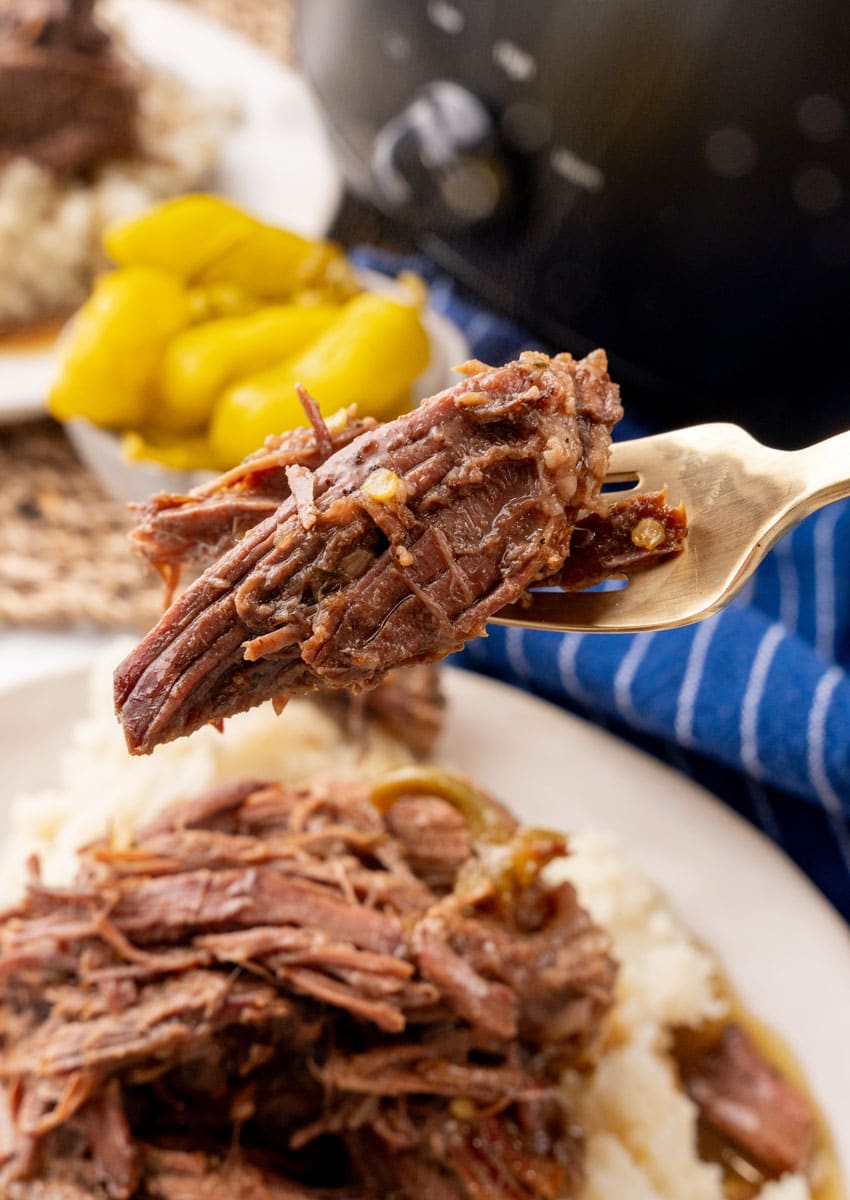 a silver fork holding up a scoop slow cooker mississippi pot roast