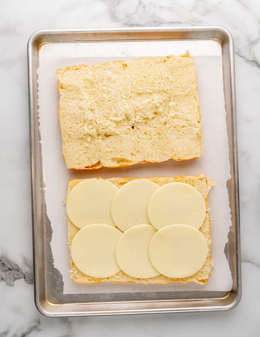 two halves of cut hawaiian rolls resting on a parchment paper lined baking sheet