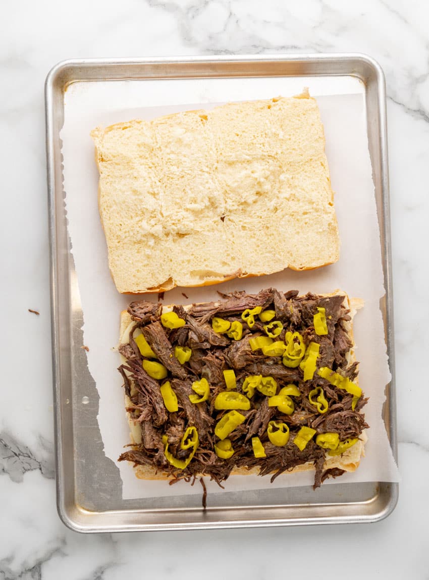 halves hawaiian rolls topped with shredded pot roast and chopped pepperoncini peppers on a parchment paper lined baking sheet