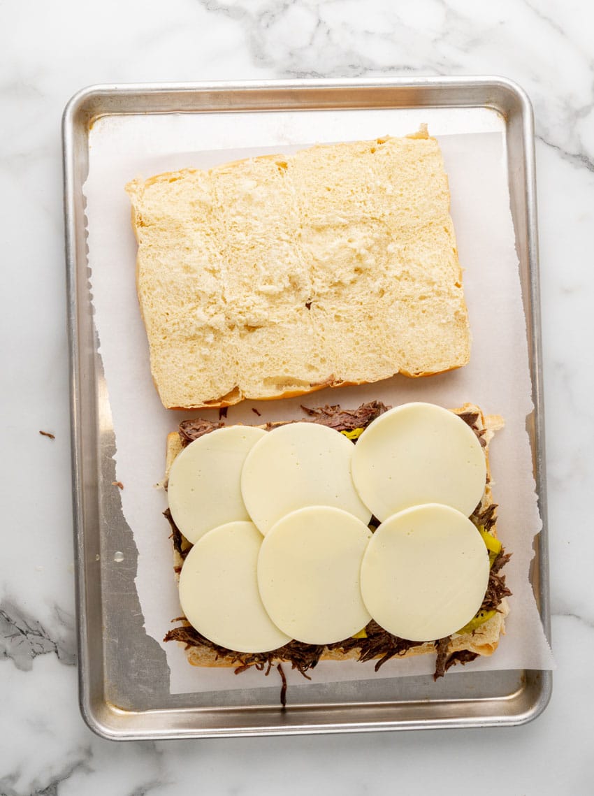 halves hawaiian rolls topped with shredded pot roast and chopped pepperoncini peppers and provolone cheese on a parchment paper lined baking sheet