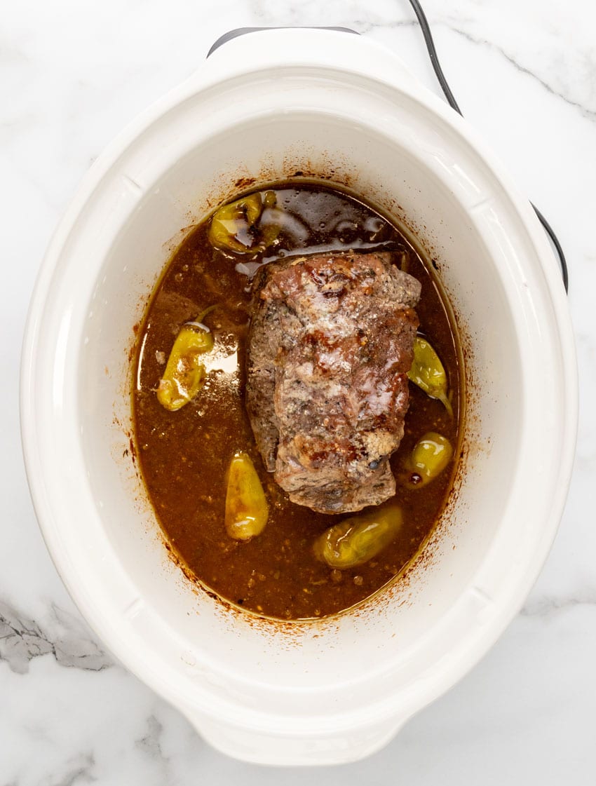 a cooked mississippi pot roast in the bowl of a white slow cooker