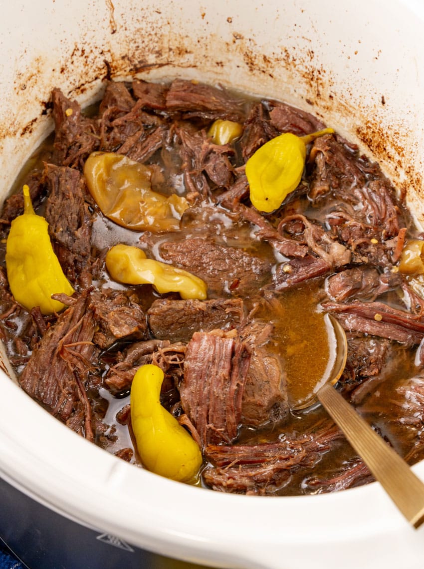 shredded mississippi pot roast and pepperoncini peppers in the bowl of a white slow cooker