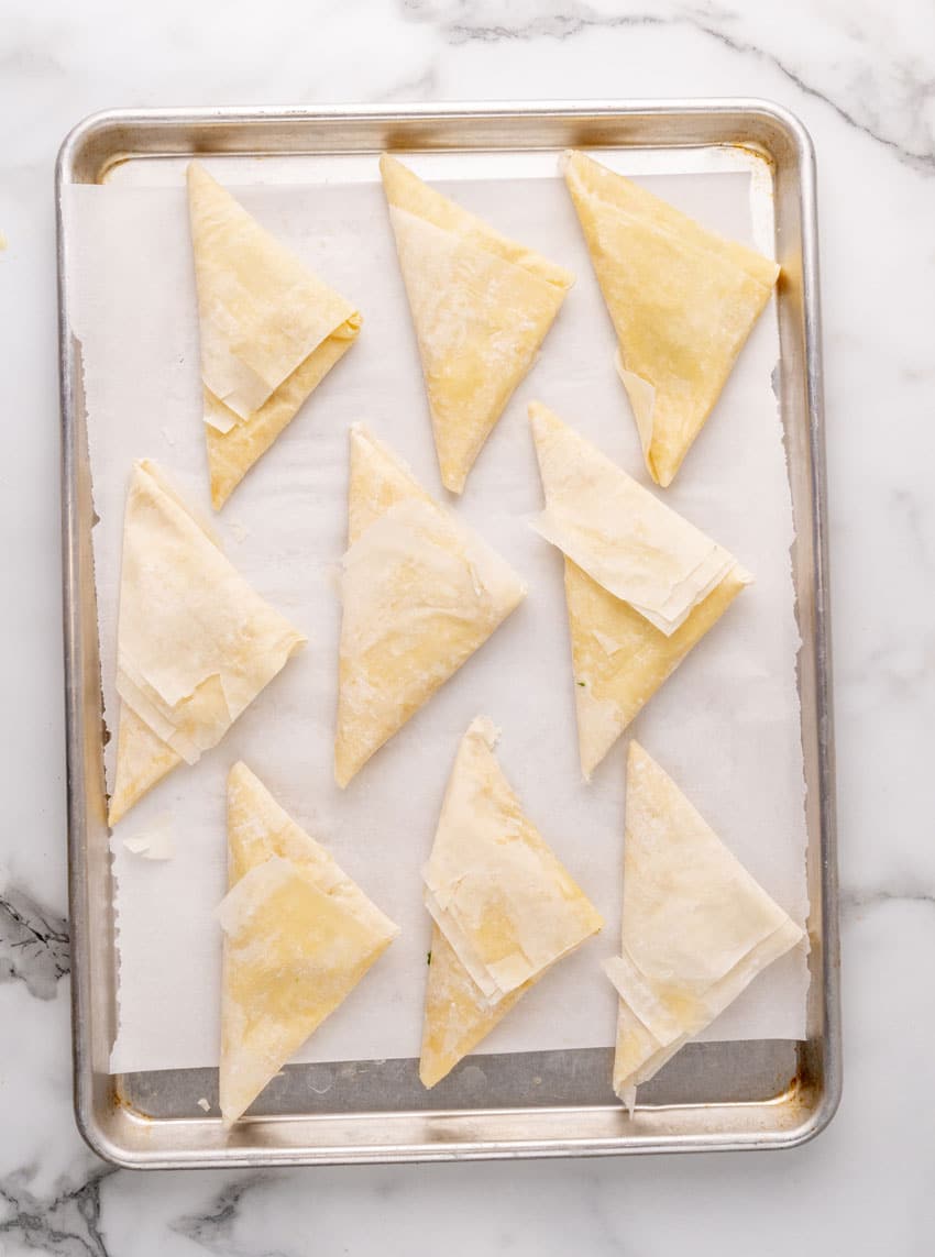 homemade spanakopita arranged in rows on a parchment paper lined baking sheet