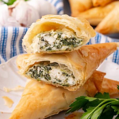 two halves of a homemade spanakopita on a small white plate with fresh herbs on the side