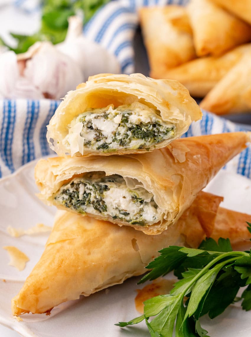 two halves of a homemade spanakopita on a small white plate with fresh herbs on the side