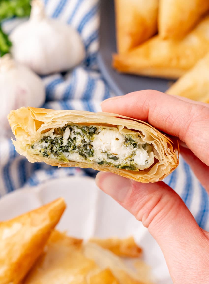 a hand holding up half a piece of spanakopita to reveal the filling inside the crispy puff pastry shell