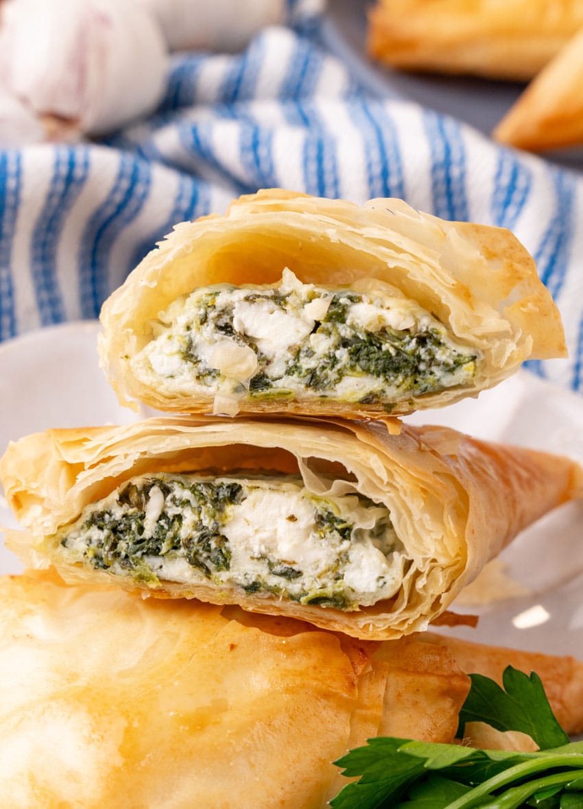 two halves of a homemade spanakopita on a small white plate with fresh herbs on the side