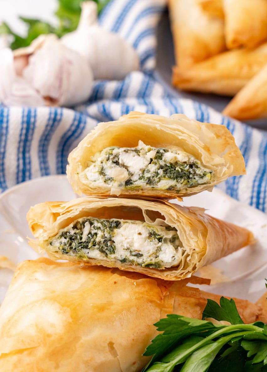two halves of a homemade spanakopita on a small white plate with fresh herbs on the side