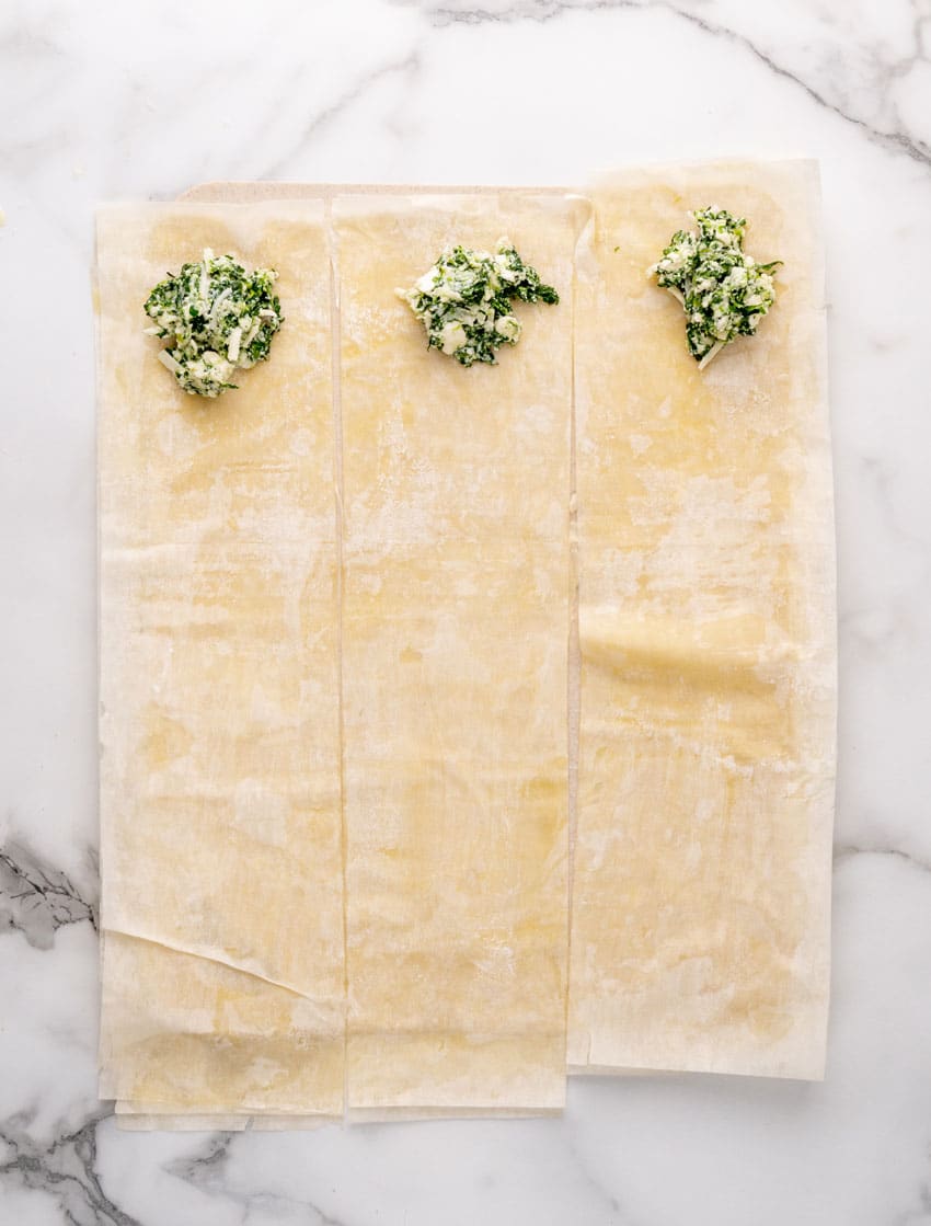 dollops of spanakopita filling at the end of three strips of puff pastry