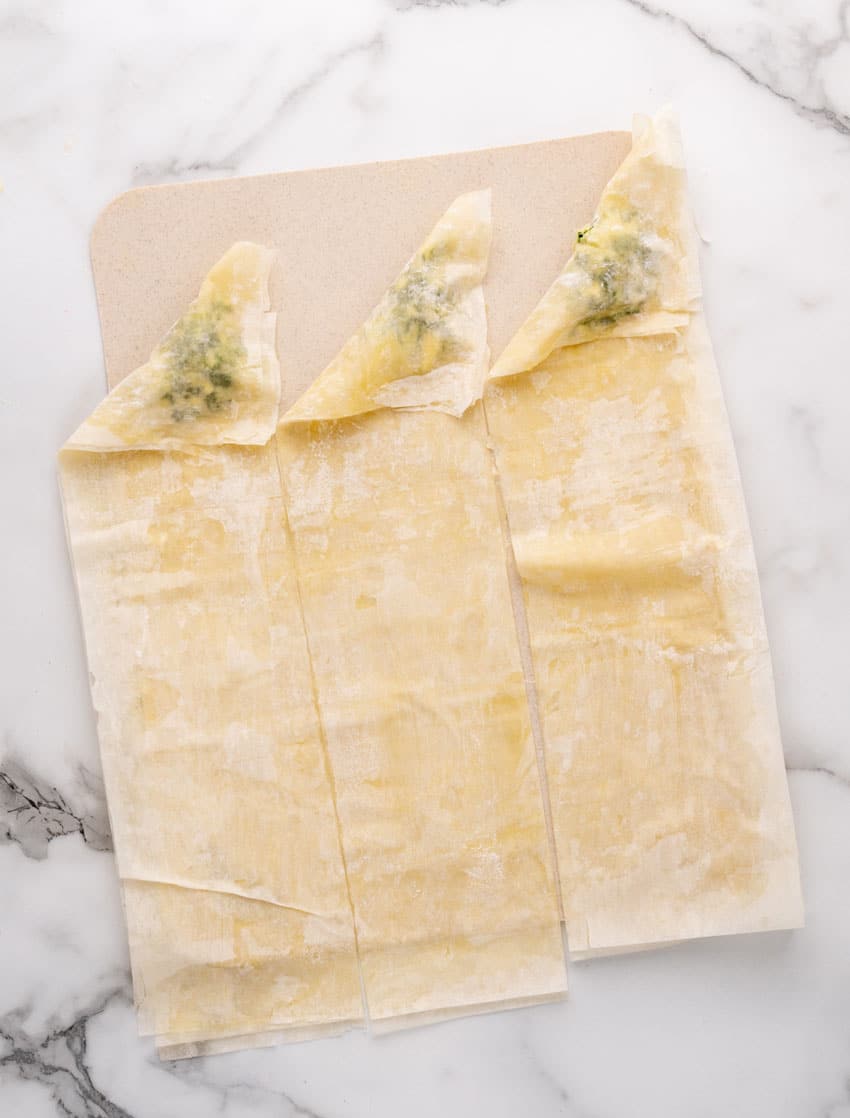 an overhead image showing how to fold homemade spanakopita strips of puff pastry