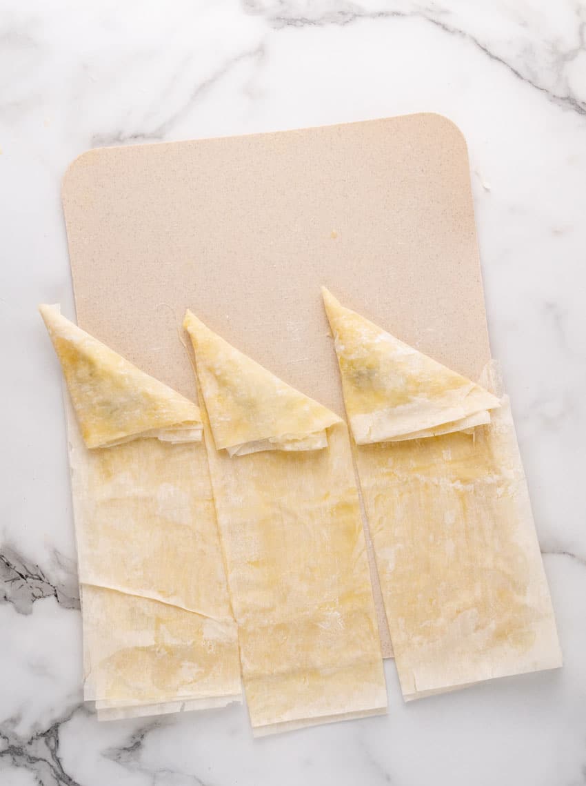 an overhead image showing how to fold homemade spanakopita strips of puff pastry